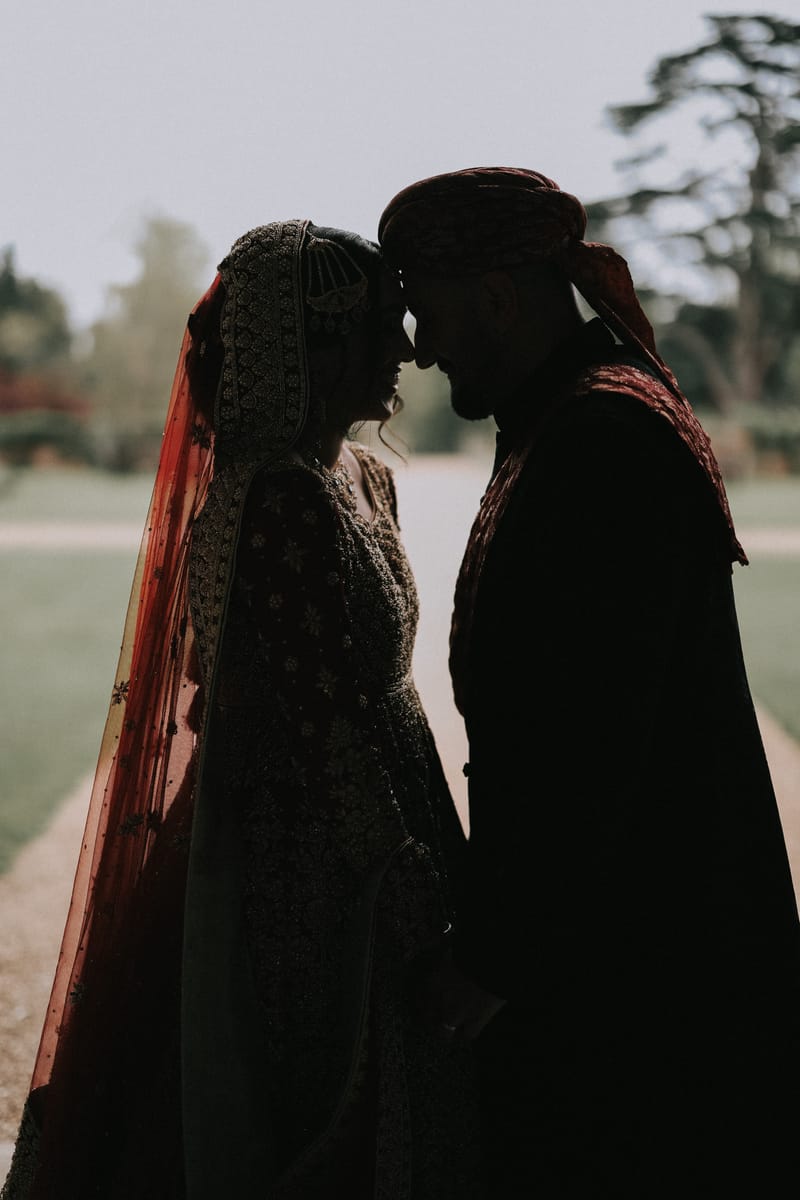 Bride and groom in silhouette, foreheads touching, against the evening sky