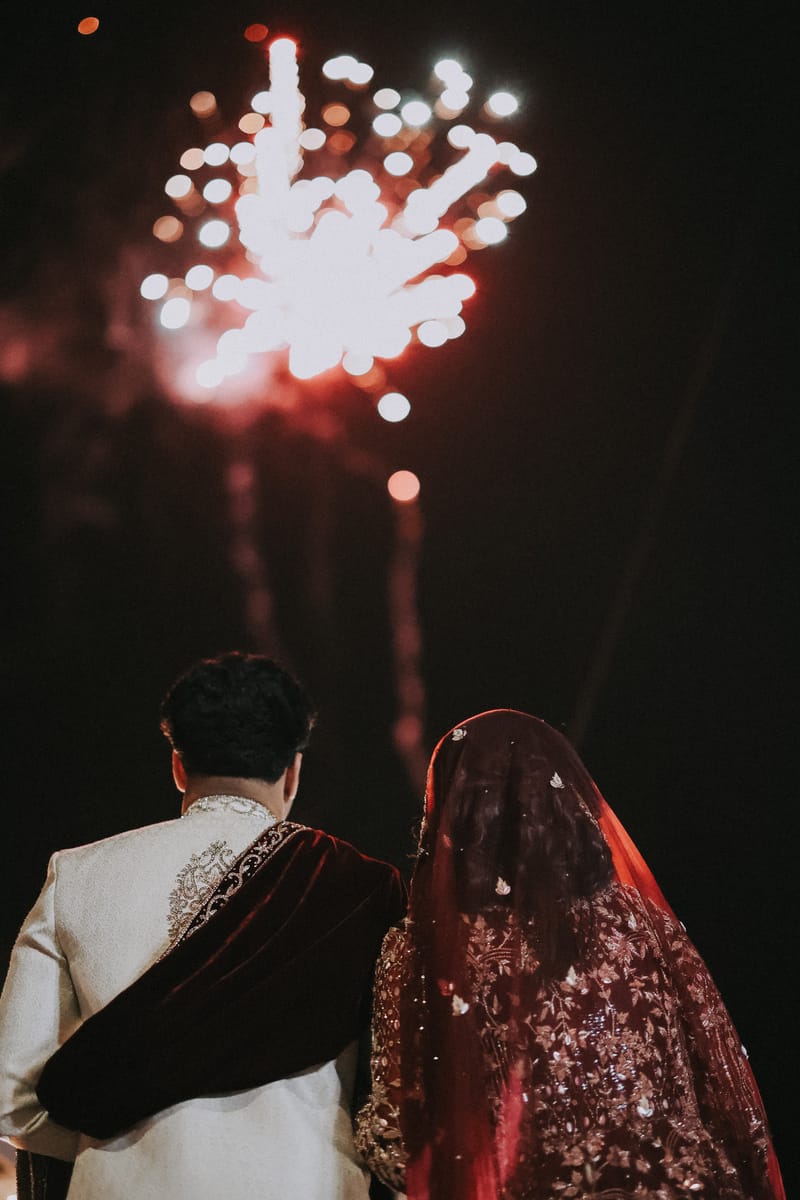 Couple seen from behind, watching fireworks light up the night sky