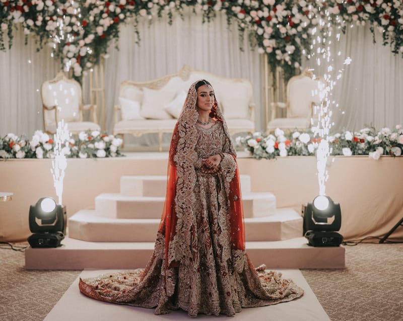 Bride in a richly embroidered lehenga in front of the stage as cold sparklers rise behind her