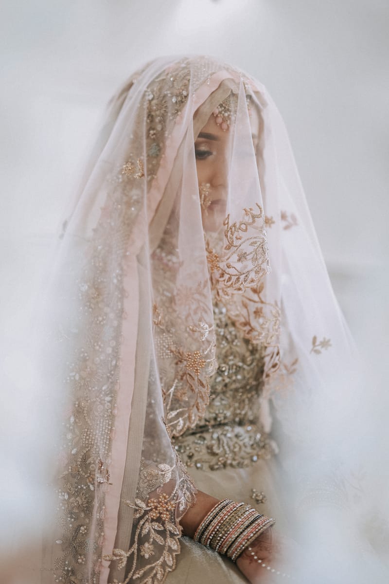 Bride beneath a sheer embroidered veil, her bangles catching the light
