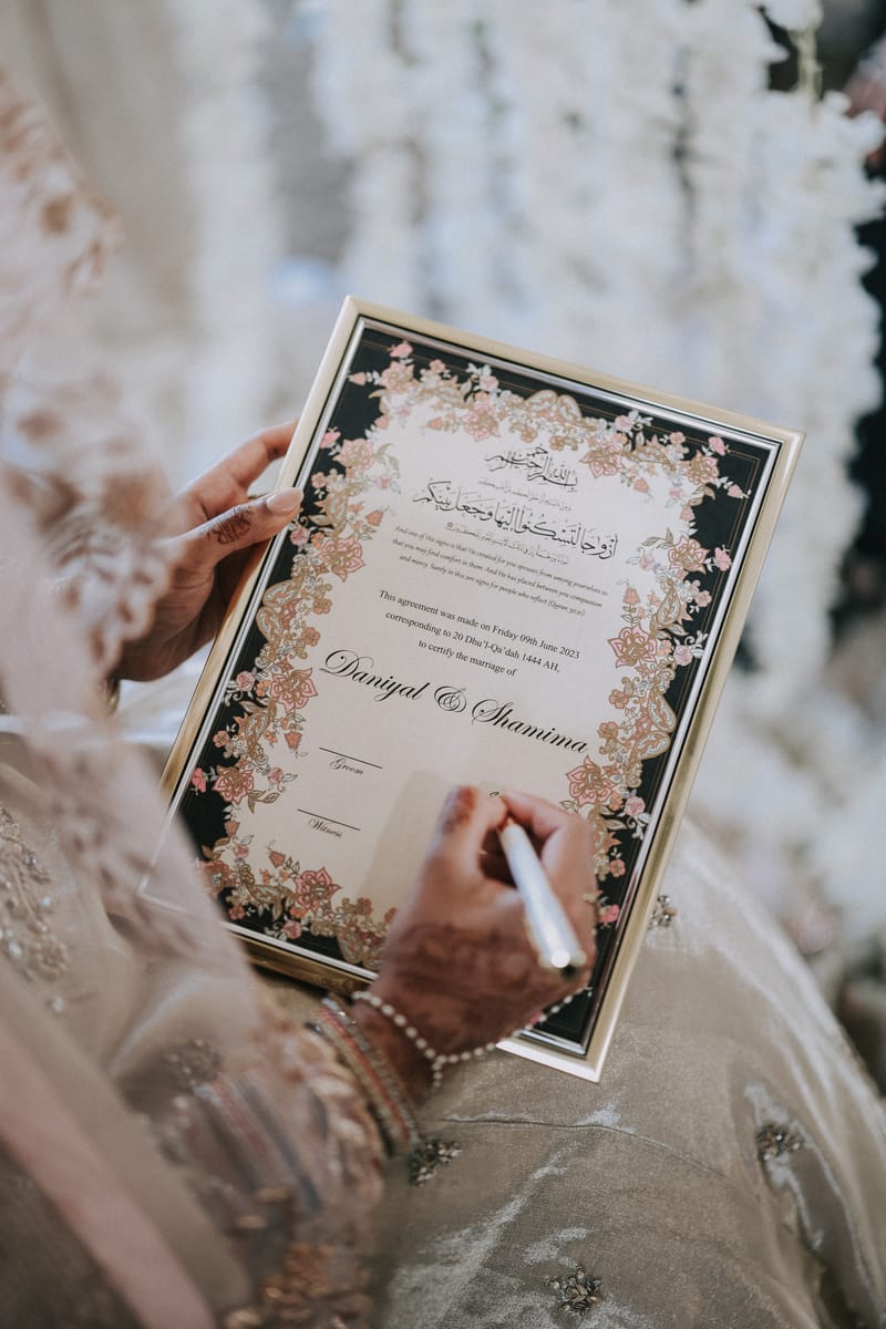 Bride with Mehndi hands signing a framed Nikkah certificate
