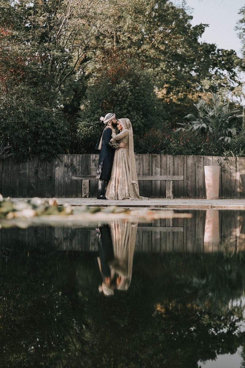 Couple embracing beside a garden pond, their reflection in the still water