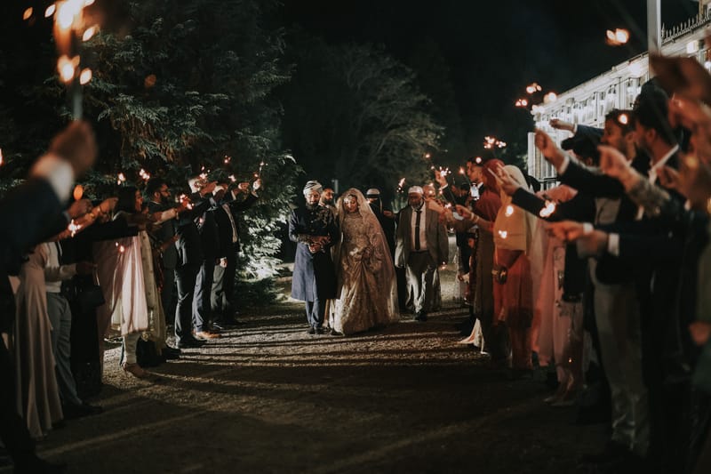 Couple walking through a tunnel of guests holding sparklers at night