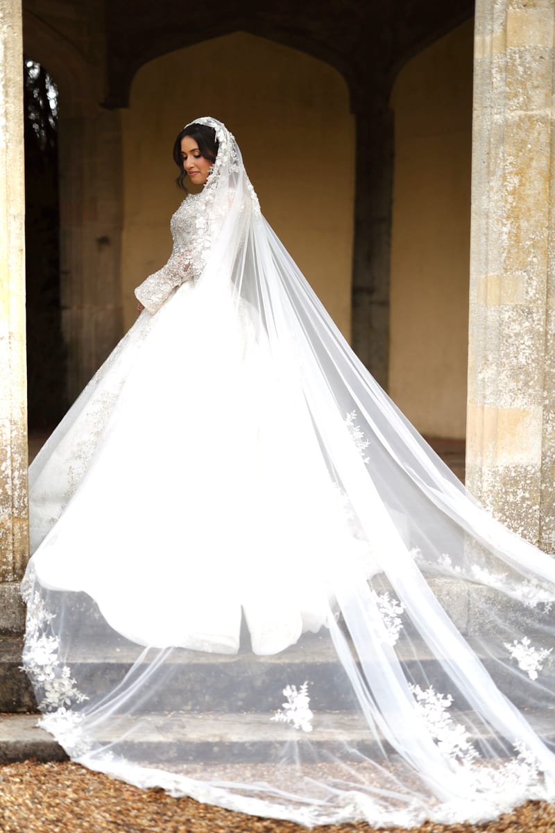 Bride in a white ball gown with a long lace-edged veil spread across stone steps