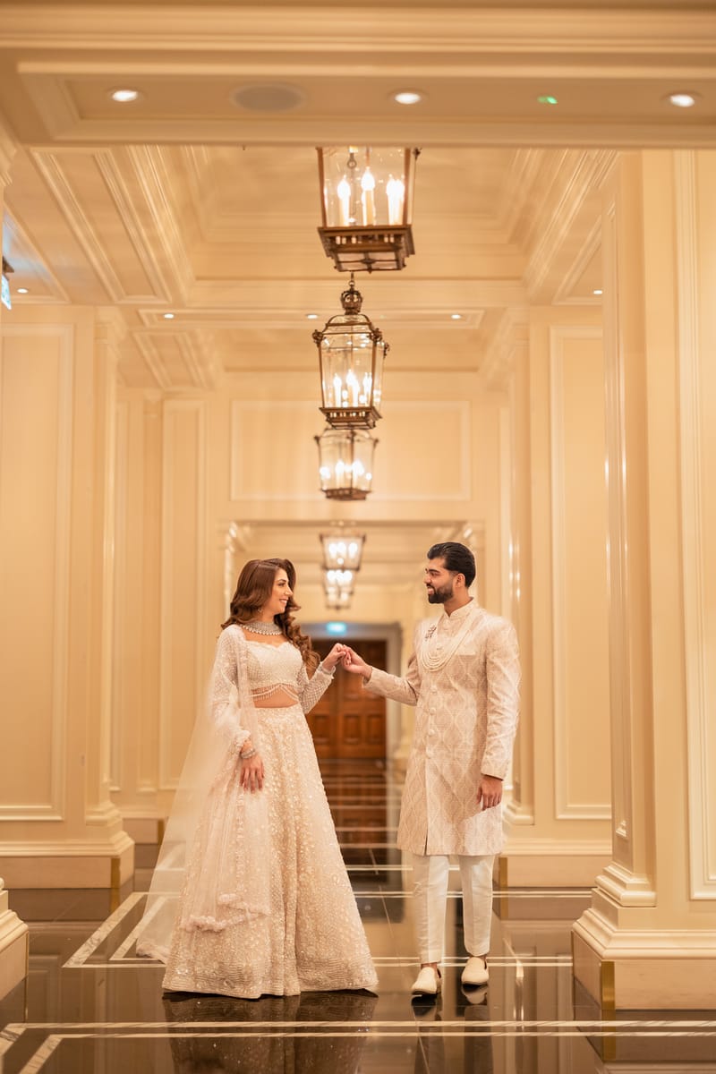 Couple in ivory holding hands in a marble corridor lit by hanging lanterns