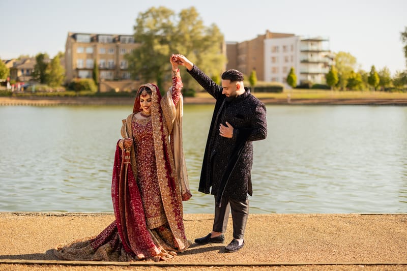 Groom twirling his bride in red and gold beside a lake