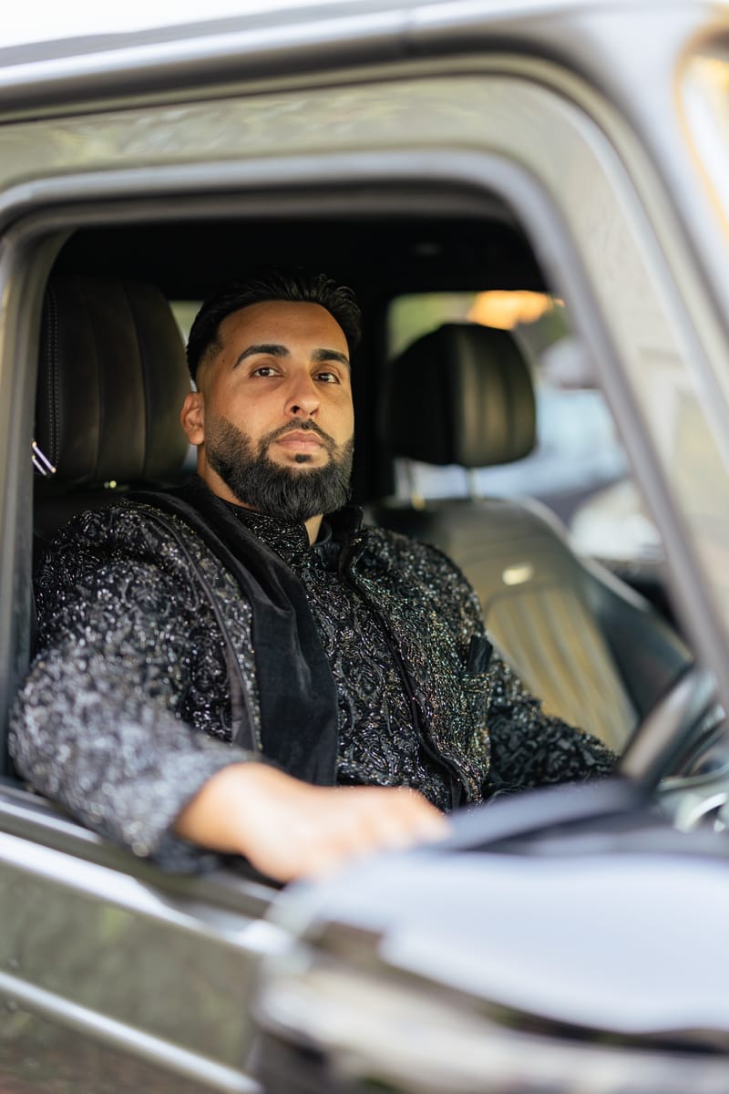 Groom in a black embellished sherwani at the wheel of a car, looking out of the window