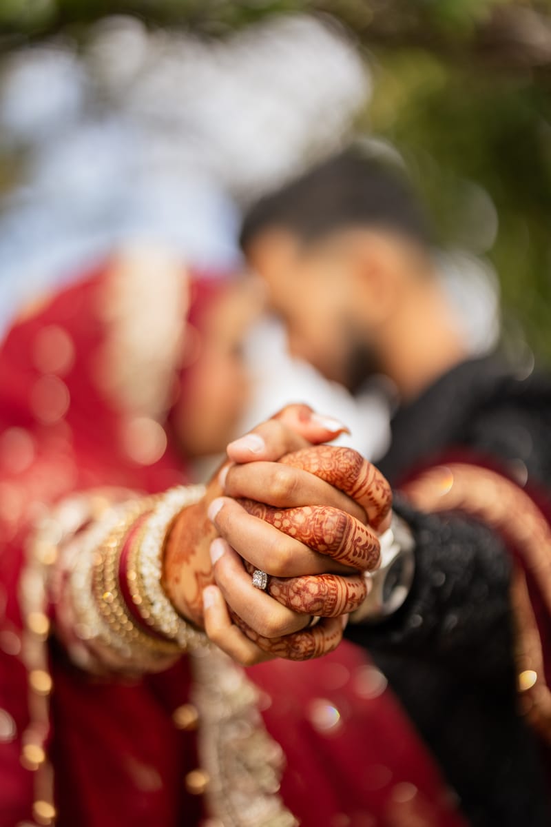 Close-up of the couple's clasped hands, her Mehndi and red and gold bangles in focus