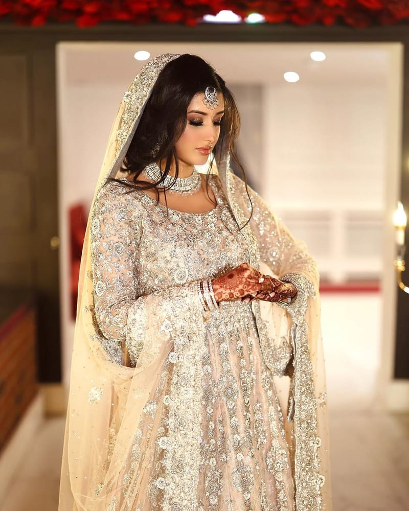 Bride in ivory and silver with a tikka and choker, looking down at her Mehndi hands